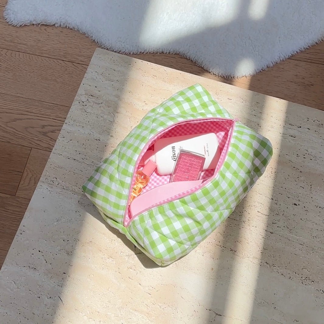 Green gingham pouch with pink-lined interior, holding makeup bottles and case