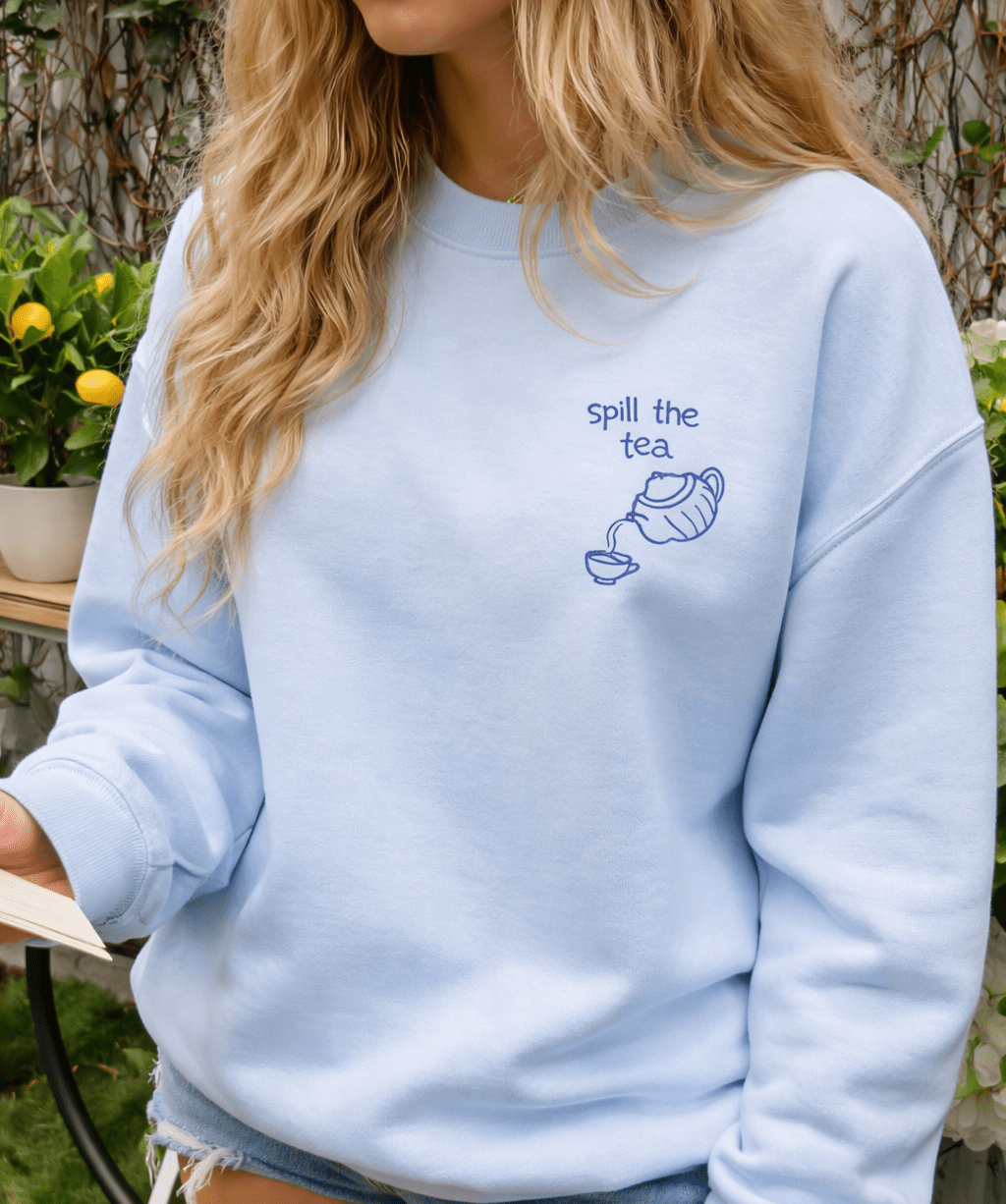 Baby blue sweatshirt on model, “Spill the tea” teapot graphic at upper chest