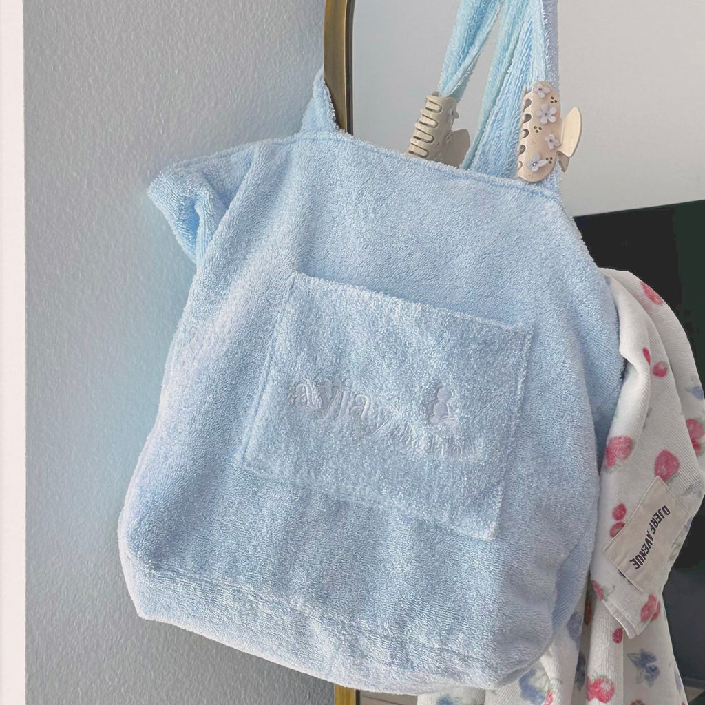 Baby blue terrycloth tote bag with wide handles and embossed front logo