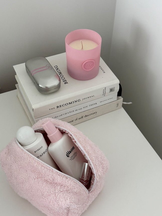 Pink teddy makeup bag with zipper open, filled with skincare bottles and lip product