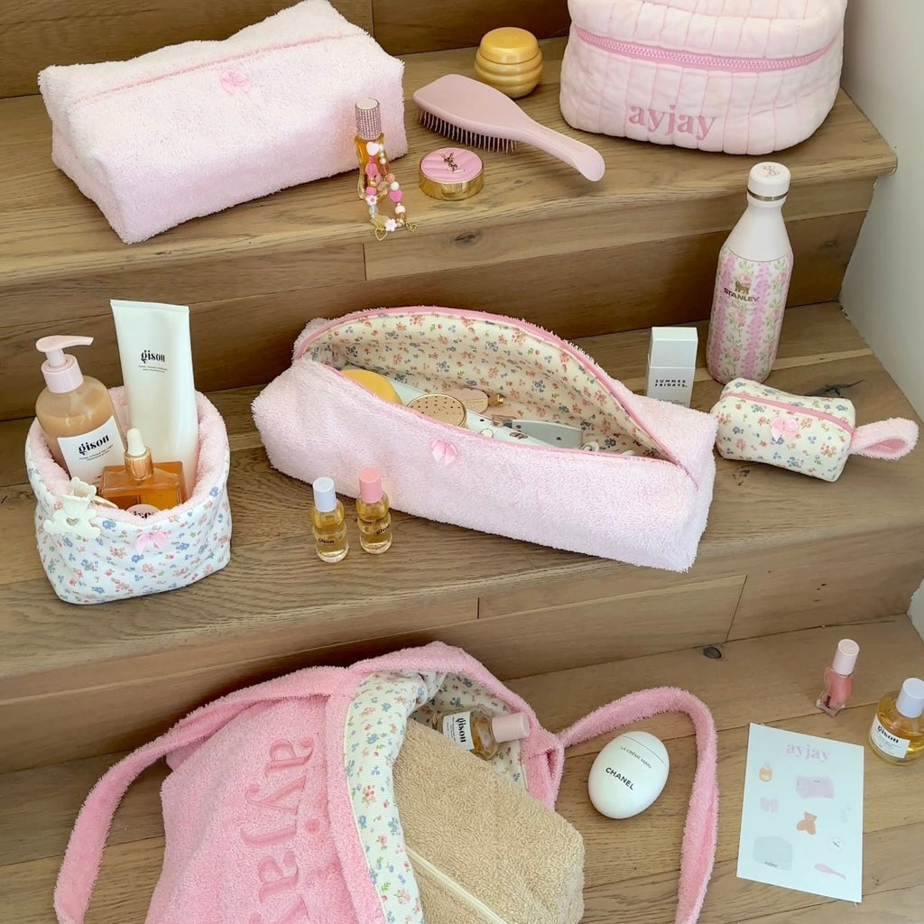 Pink terrycloth toiletry pouch with floral lining, zip top, and bow accents