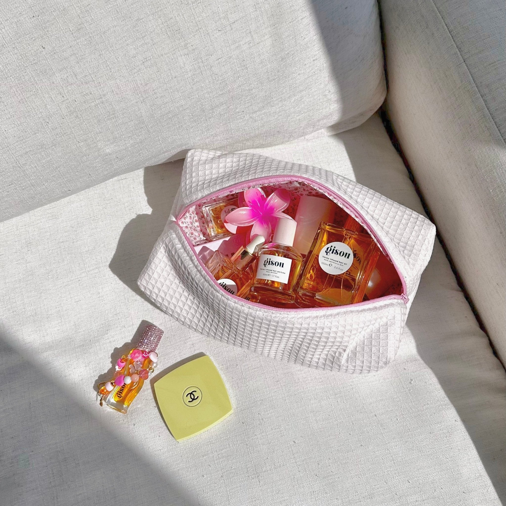 White waffle-knit zip pouch with pink lining and flower decor, open with bottles inside