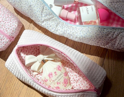 White waffle-knit cosmetic pouch with pink zipper, open floral interior and bow detail