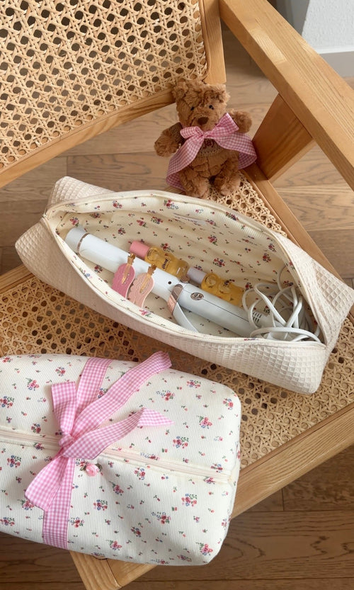 Beige waffle-texture oval pouch with floral lining and pink gingham bow; holds bottles