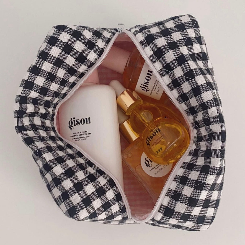 Black-and-white gingham makeup pouch opened with bottles and cream jars inside