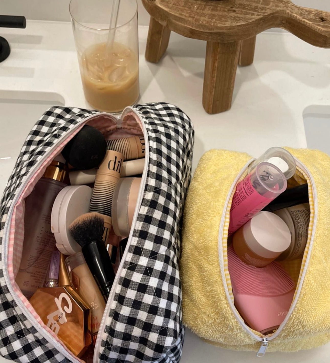 Black-and-white gingham zip pouch opened; cosmetics and brushes visible inside