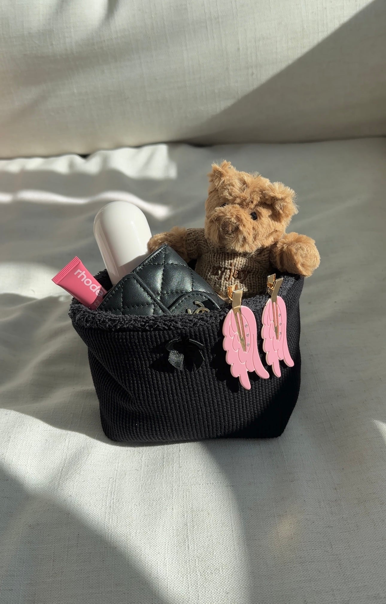 Black waffle-knit organizer basket with plush rim and pink angel wing charm, holding teddy