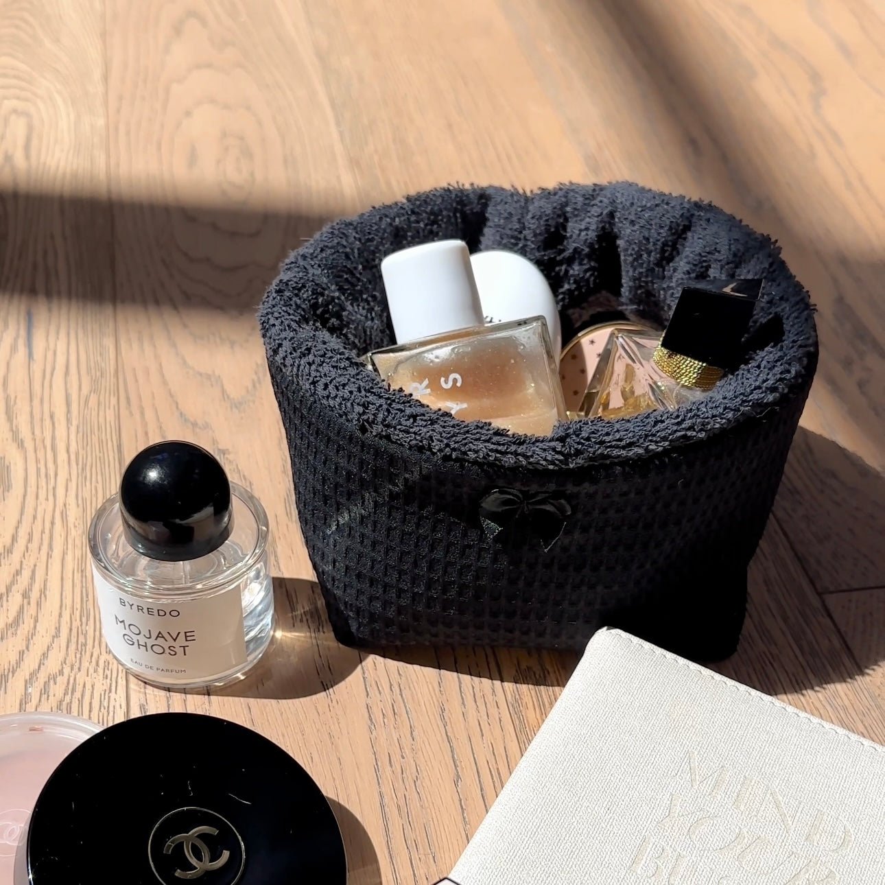 Black waffle-knit organizer basket with plush rim, perfume bottles inside; bow accent