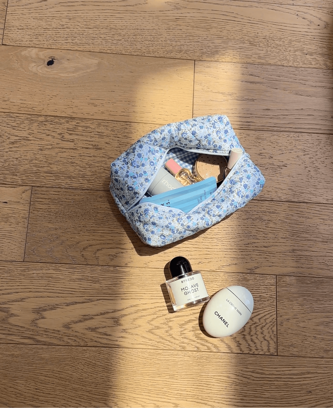 Blue floral zippered pouch open on wood floor with toiletries inside