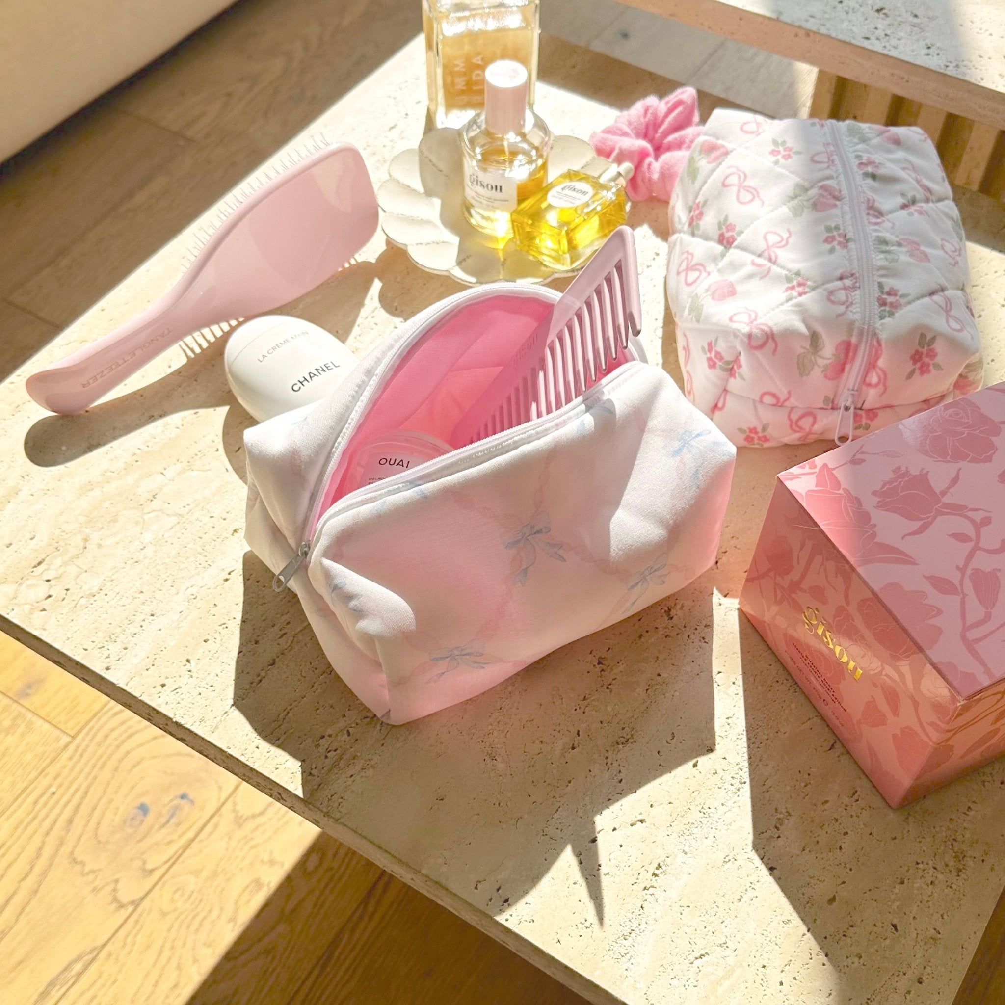 White zip pouch with pink bow print and curved shape on tabletop