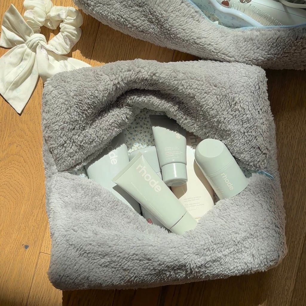 Grey teddy pouch with blue zipper trim, open with mint-colored skincare bottles inside