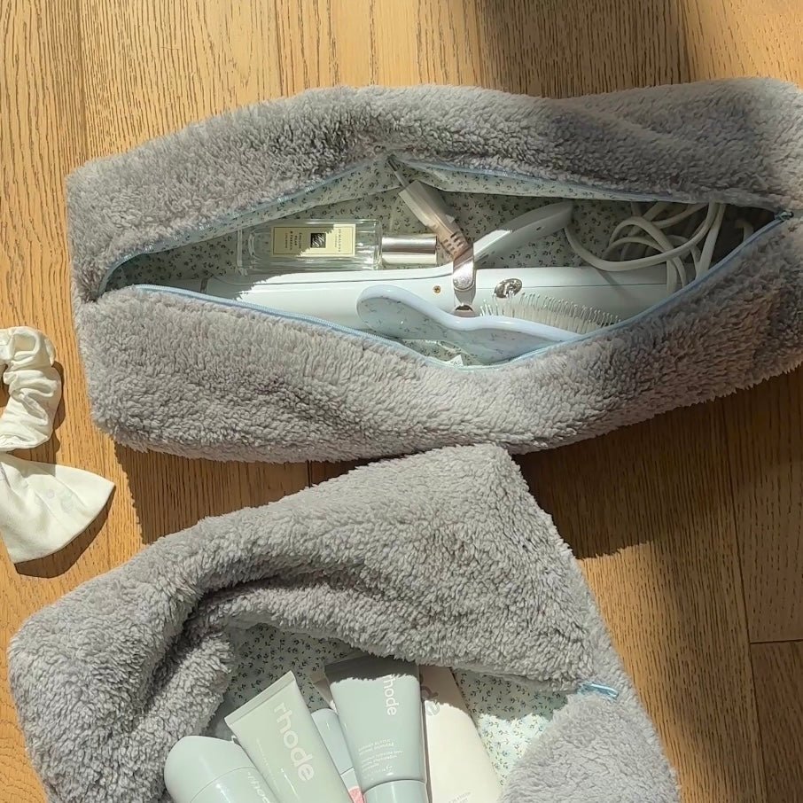 Light grey teddy pouch with blue zipper trim, open with hair products and cord inside