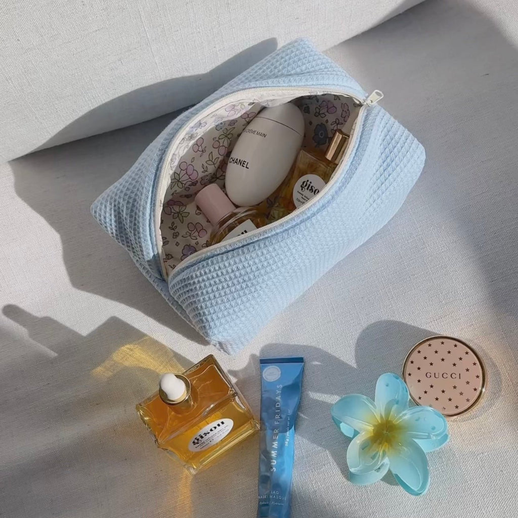 Light blue waffle-knit zip pouch with zipper, displayed on table with bottles