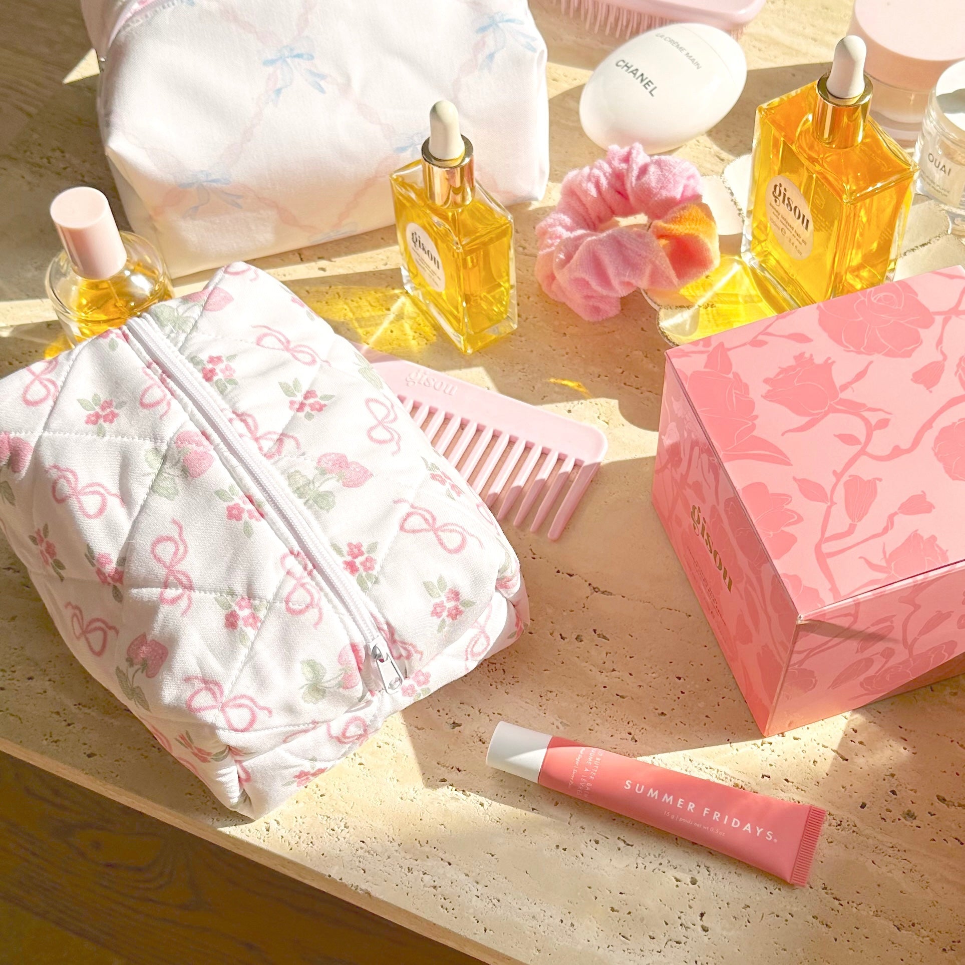 White bow-and-flower zip pouch with pink trim, on table with beauty bottles and brush
