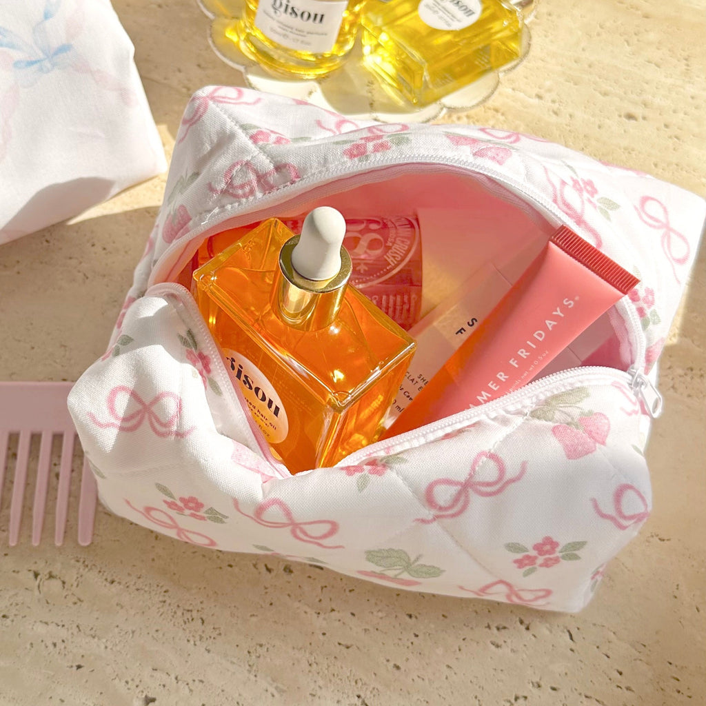 White pouch with pink bow pattern, open front showing perfume bottles and cards