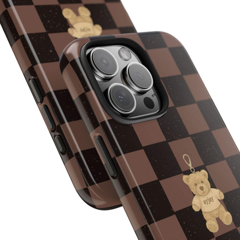 Angled view: brown checkered phone case with teddy bear, camera lens cutout and side buttons