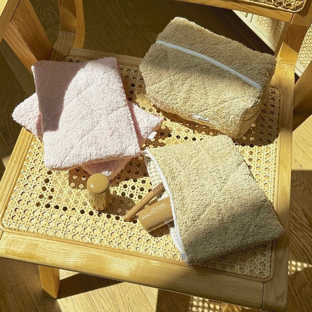 Assorted teddy pouches in beige and light colors on a woven tray, zip openings visible