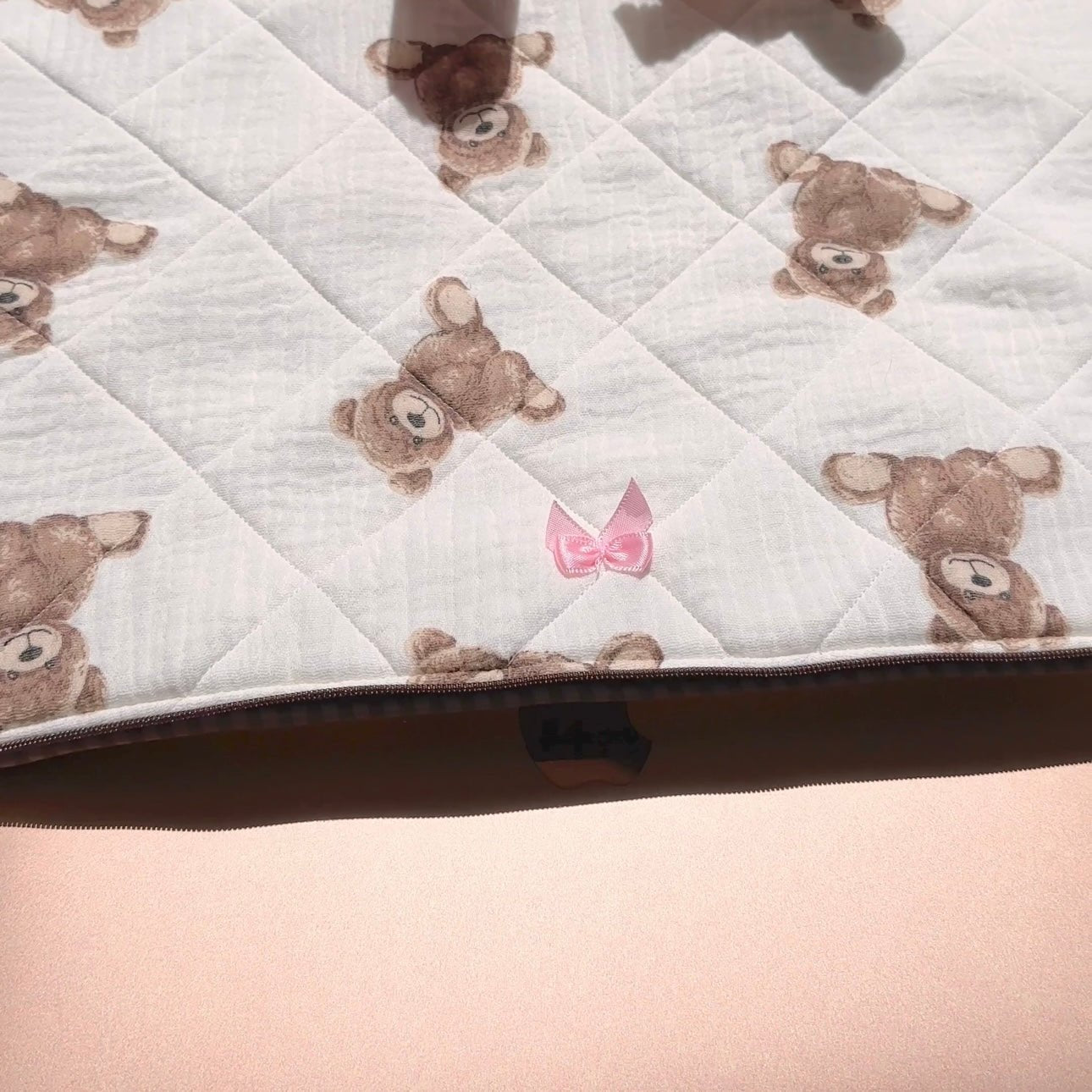 Close-up quilted white sleeve with teddy faces and small pink bow near zipper
