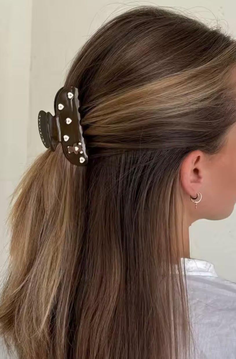 On hair: dark brown claw clip with teddy bear and heart accents, side hold