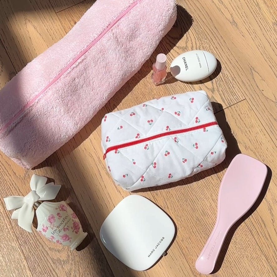 Cherry-print zip pouch with red trim, beside pale pink towel wrap and vanity items
