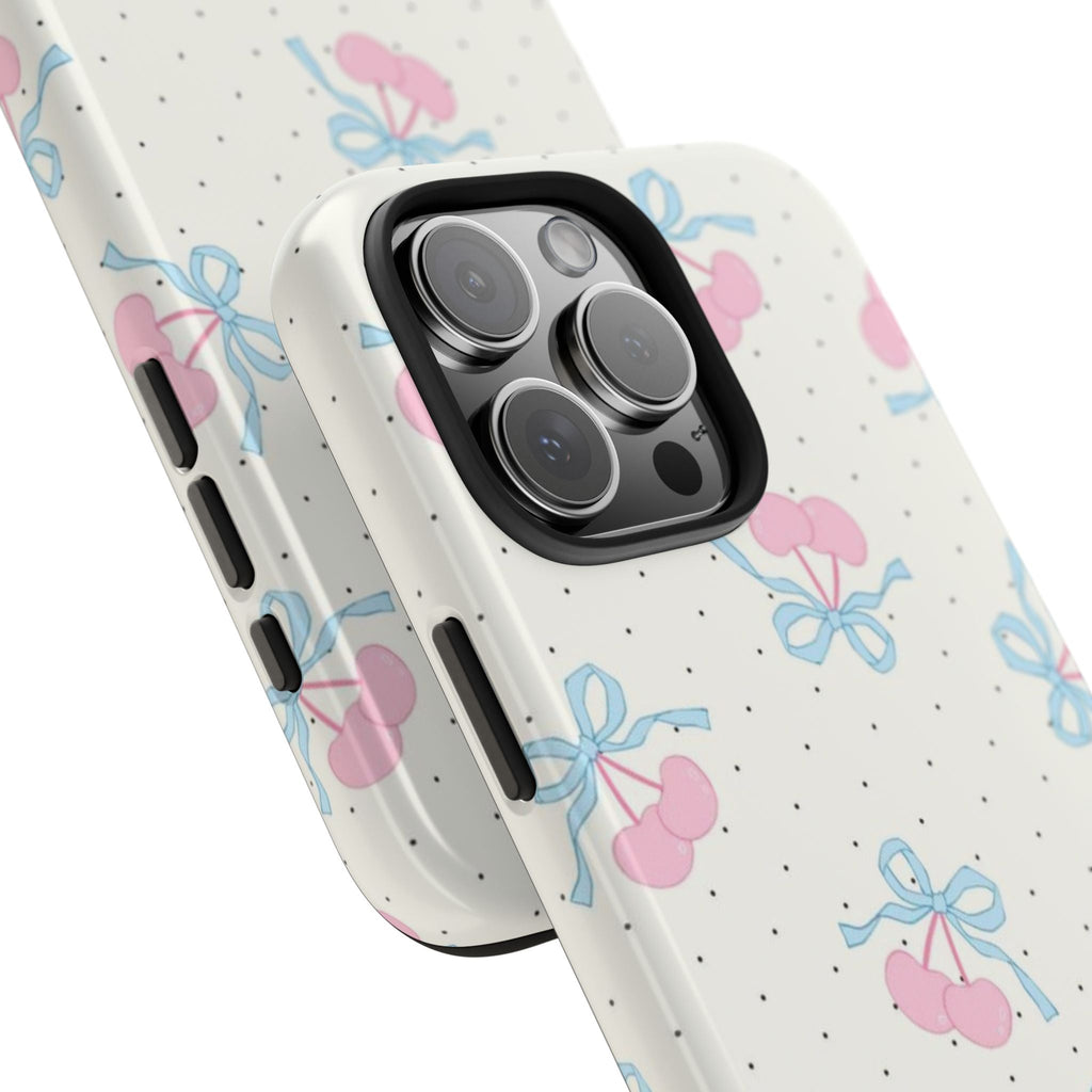 Angled view of white phone case with pink cherries, blue bows, black polka dots; side buttons