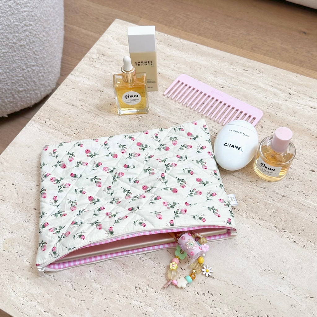 Cream floral zip pouch with pink trim lying flat, small charm keychain attached