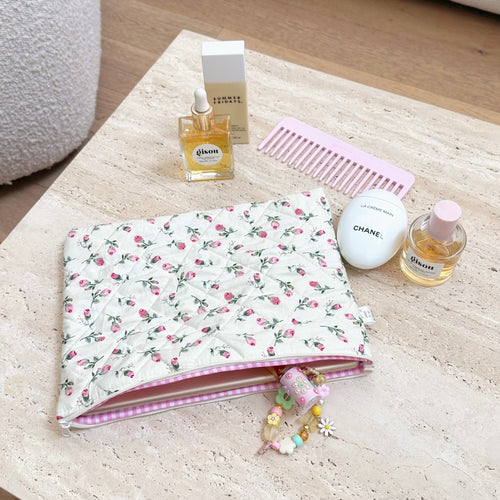 Cream floral zip pouch with pink trim lying flat, small charm keychain attached
