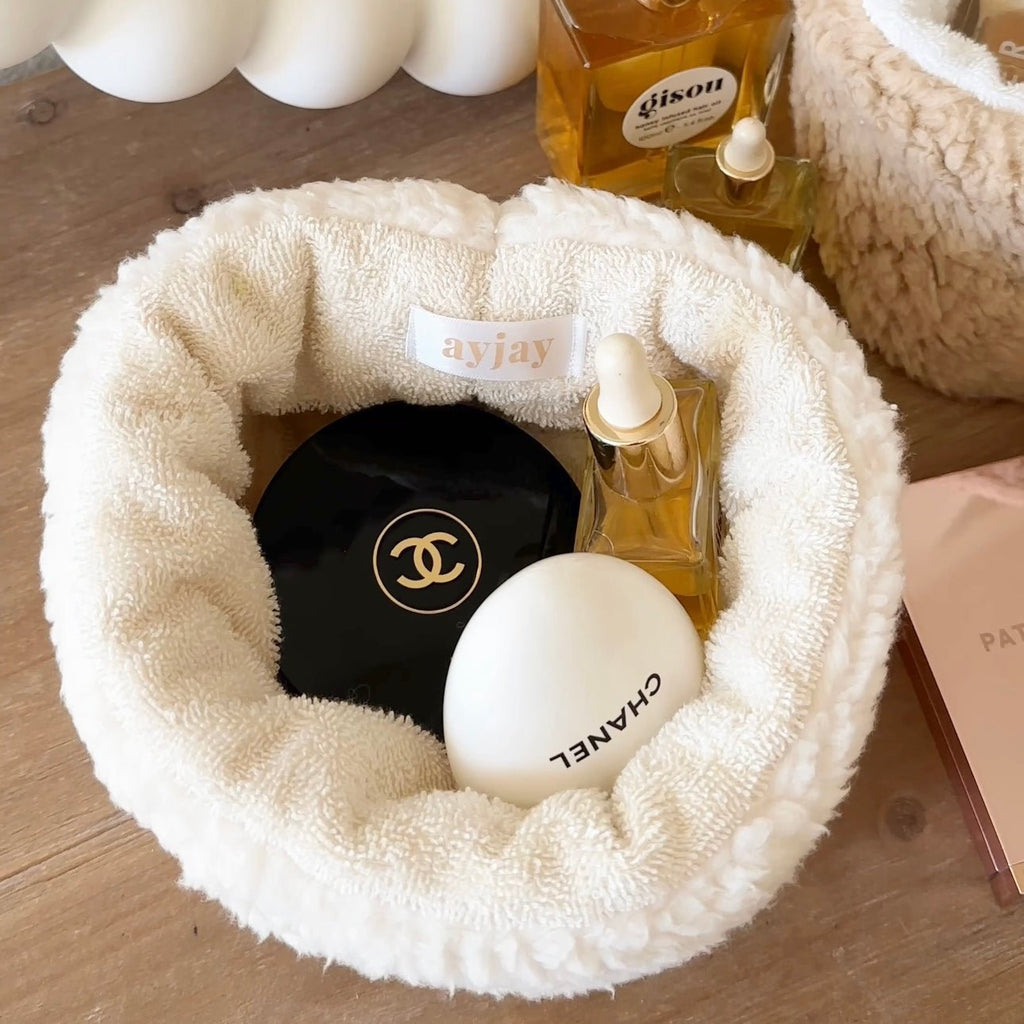 Cream teddy round organizer bowl holding small dark bottle, golden perfume, and candle