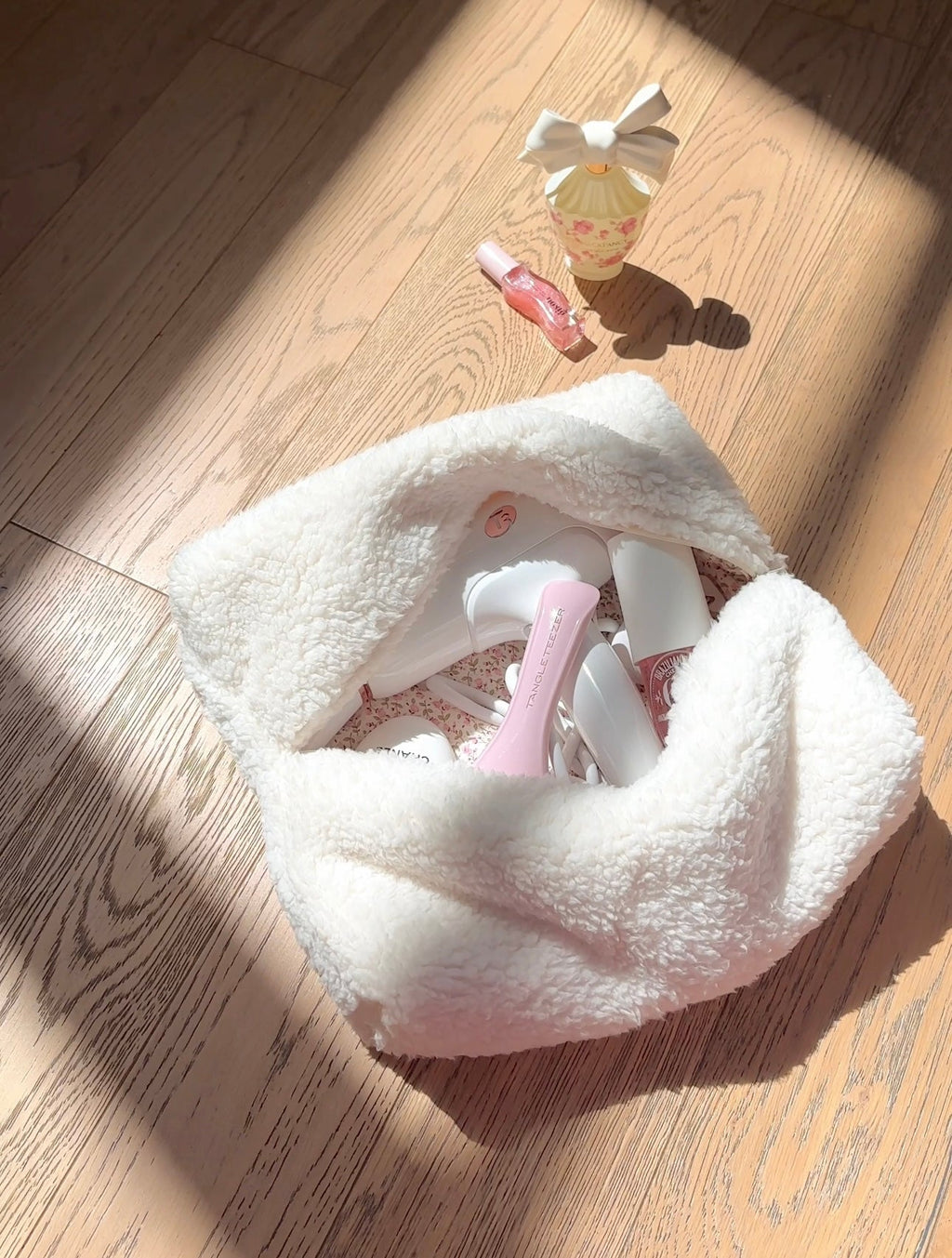 Cream teddy pouch with pink floral lining, zipper opening facing up on wood floor
