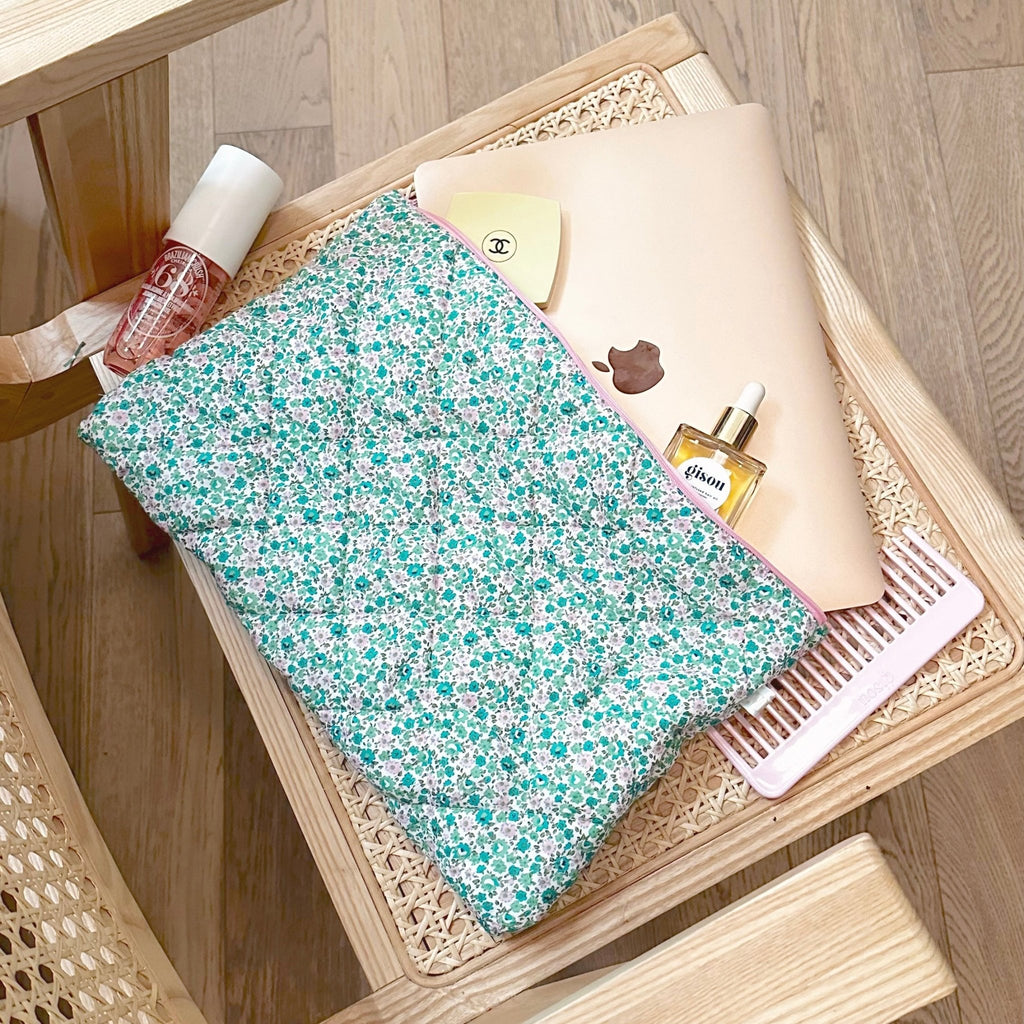 Green floral pouch with pink zipper trim on a wooden tray, partially filled with bottles