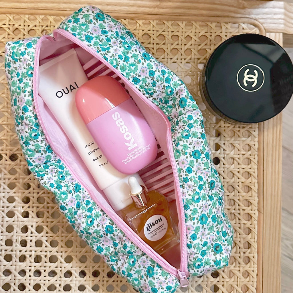 Green and pink floral zip pouch open, pink trim, holding a bottle and lotion tube