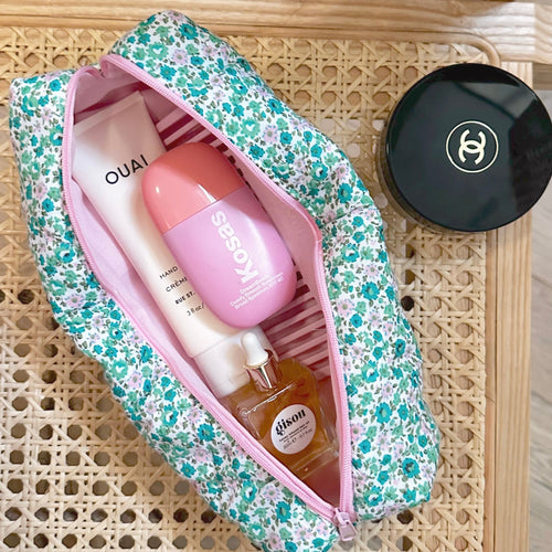 Green and pink floral zip pouch open, pink trim, holding a bottle and lotion tube