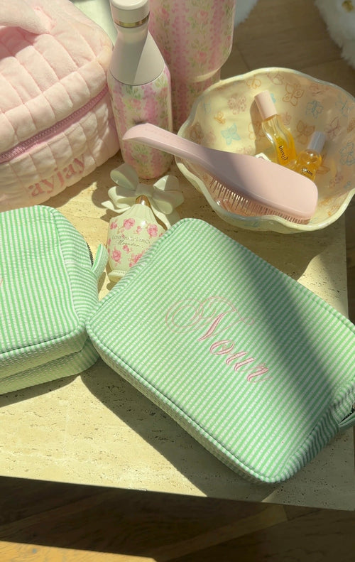 Green striped zipped pouch bag with embroidered name on front panel; quilted texture.