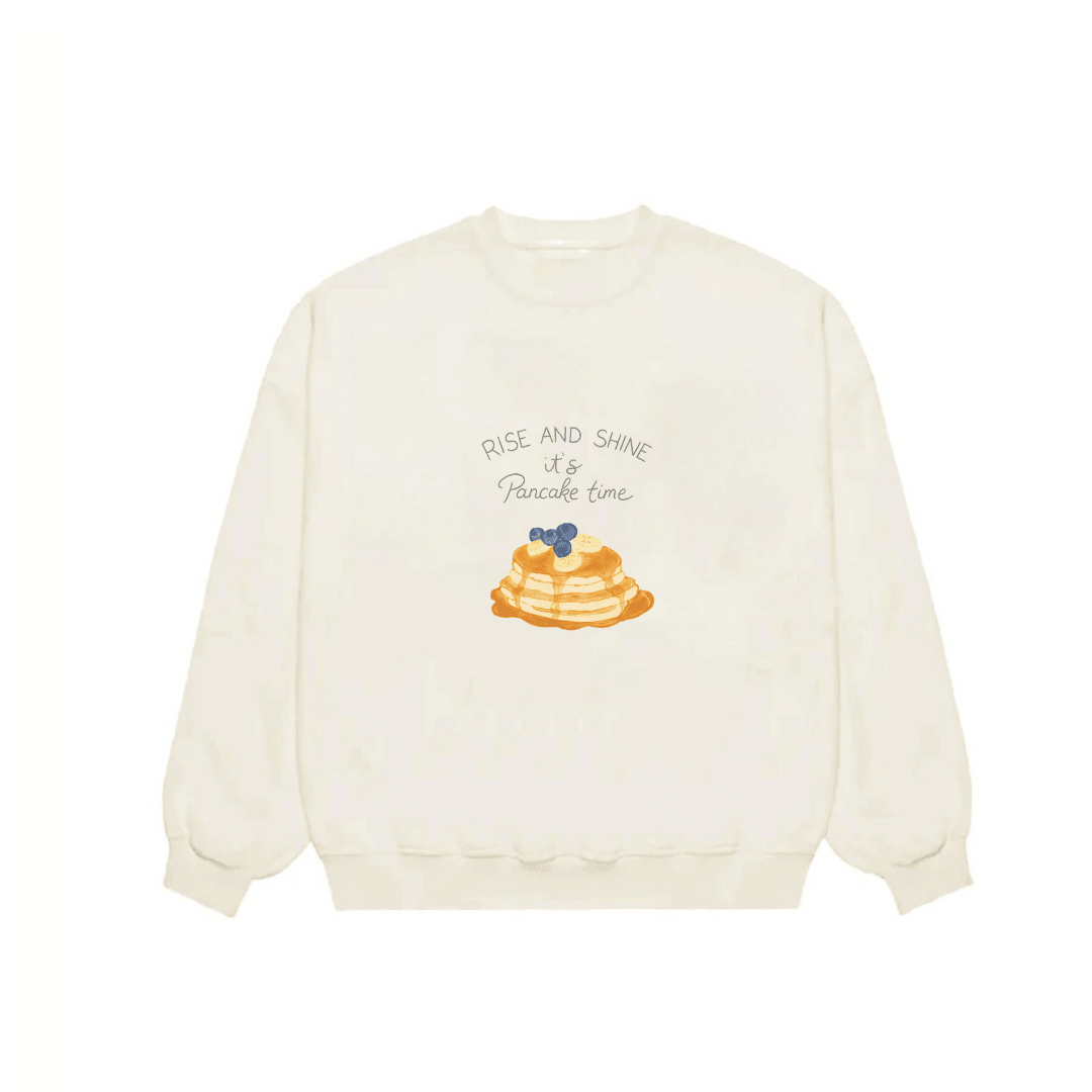 Ivory crewneck sweatshirt front view with 'Rise and Shine' pancake graphic