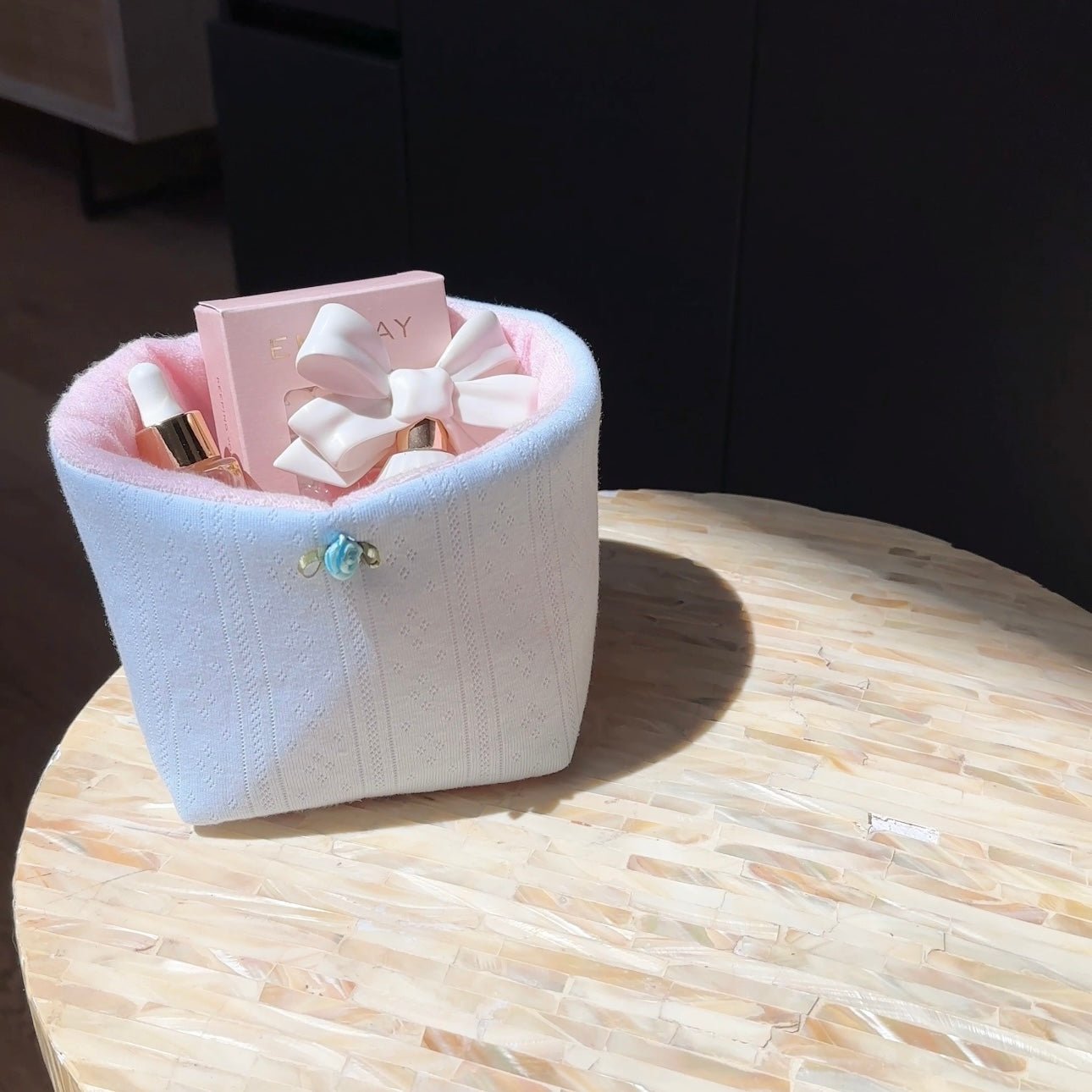 Light blue knit organizer bin with central bow and clasp, holding boxed items