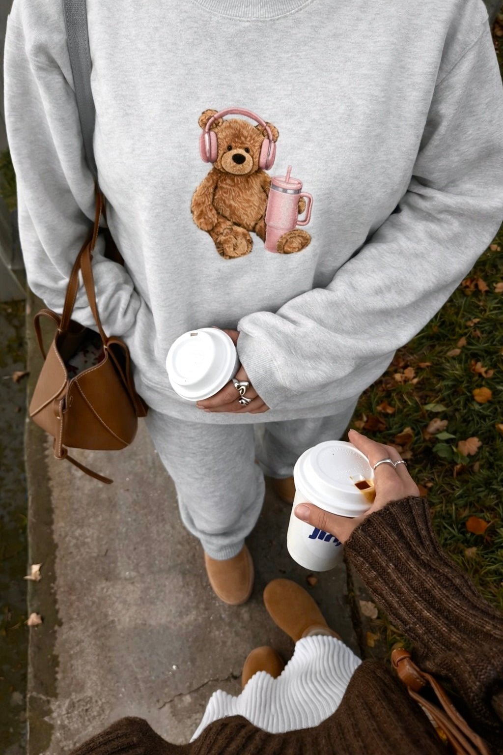 Light gray crewneck sweatshirt with teddy bear graphic wearing headphones and holding drink