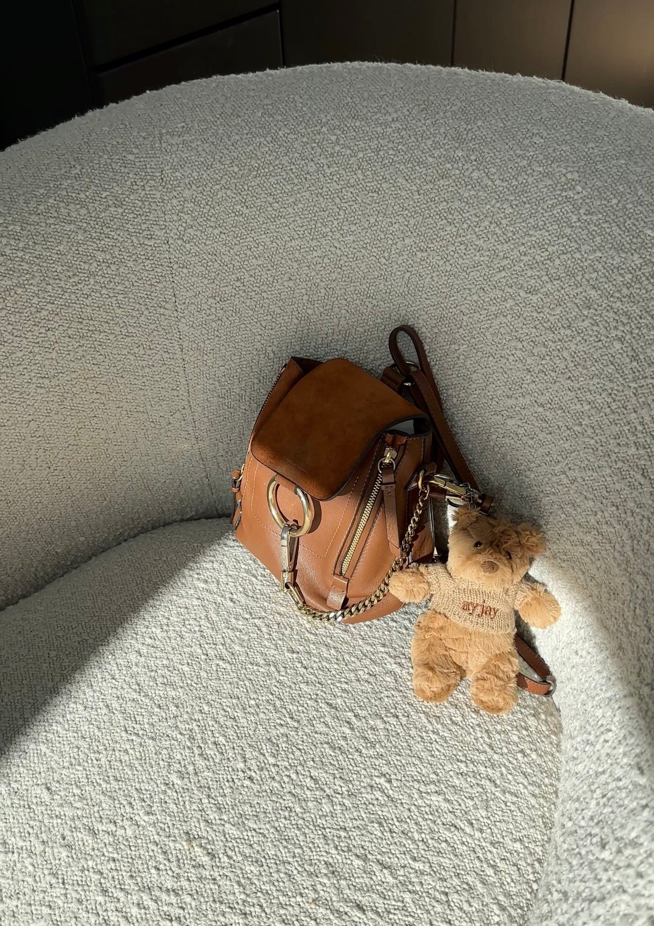Tan plush bear keychain dangling from brown mini bag, metal loop and clasp