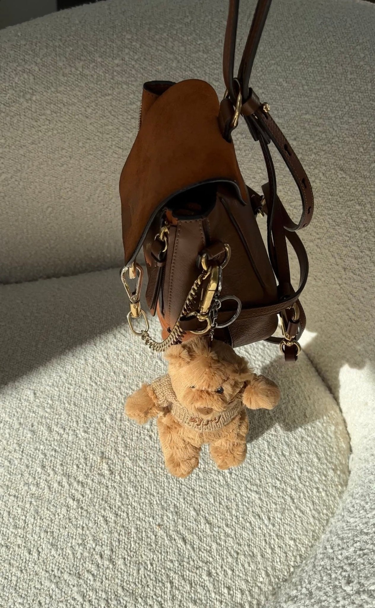 Tan bear plush keychain dangling from brown bag strap with metal clasp