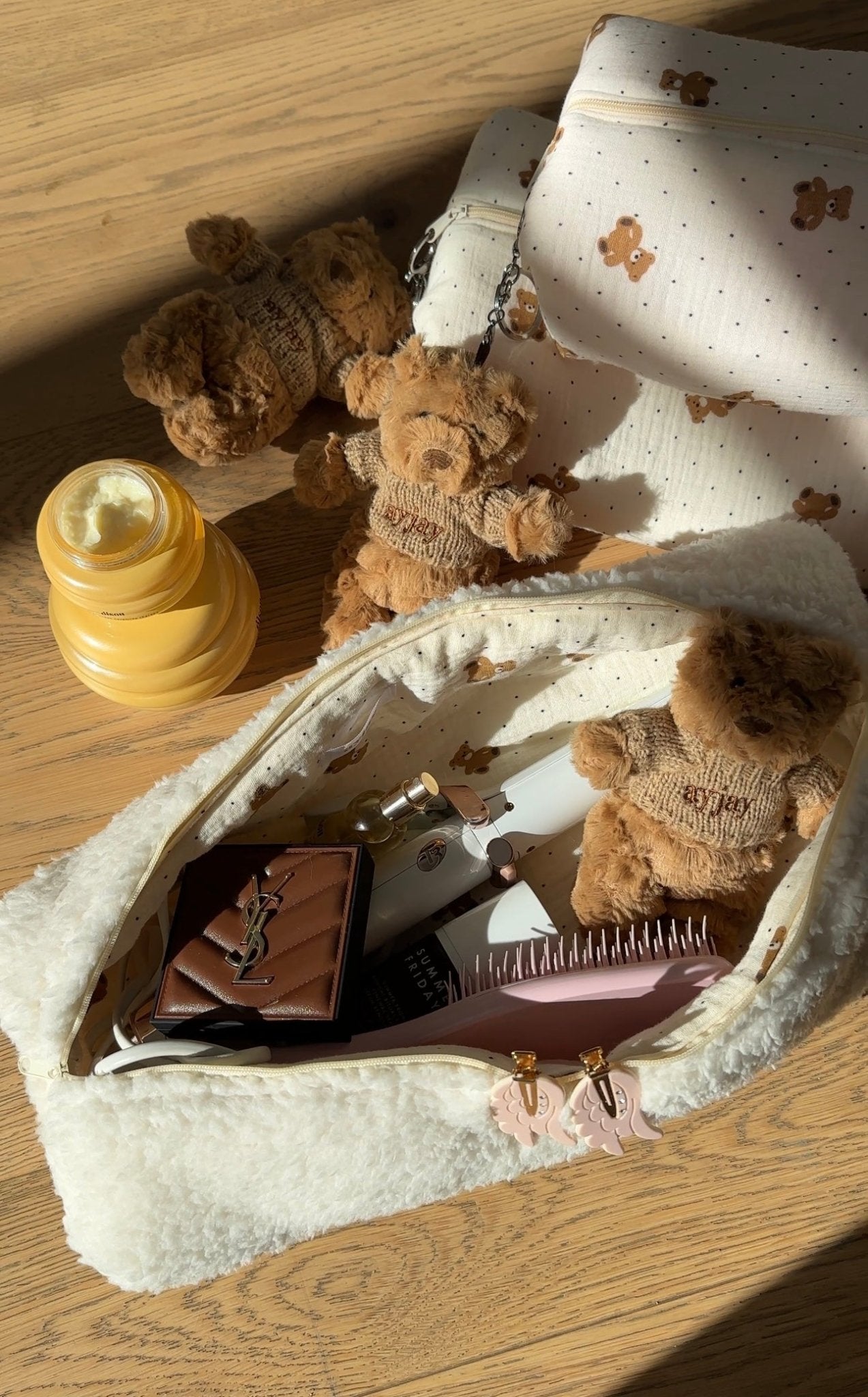 Tan plush bear keychain on white patterned pouch, metal ring and sweater visible