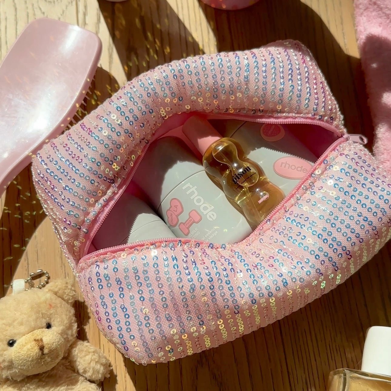 Open pink sequin zipper pouch with small bottles and items inside