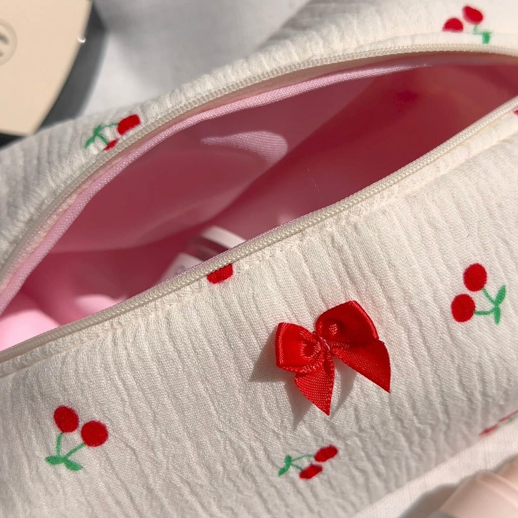 Close-up of white zip pouch with red bow and cherry embroidery on pink lining
