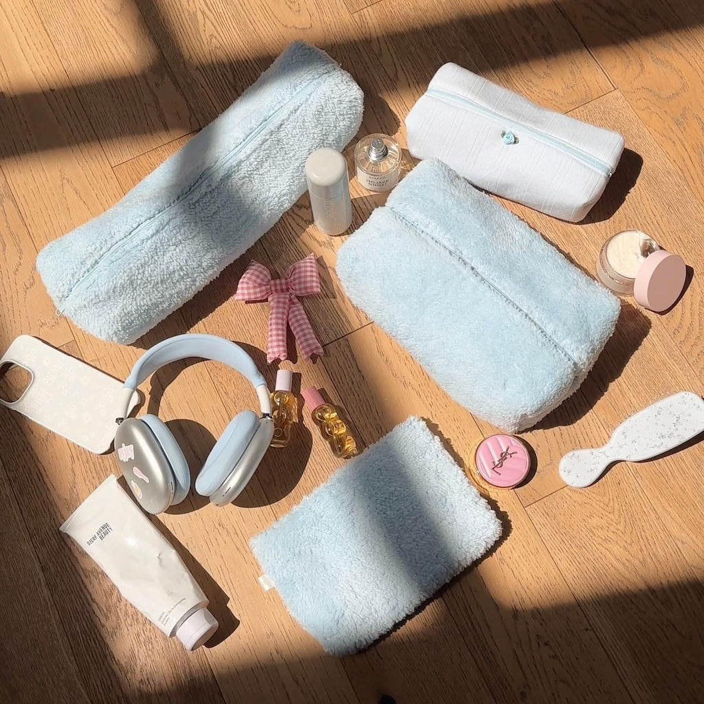 Light blue teddy plush zip pouch, folded/stacked with other plush pieces and zipper trim.