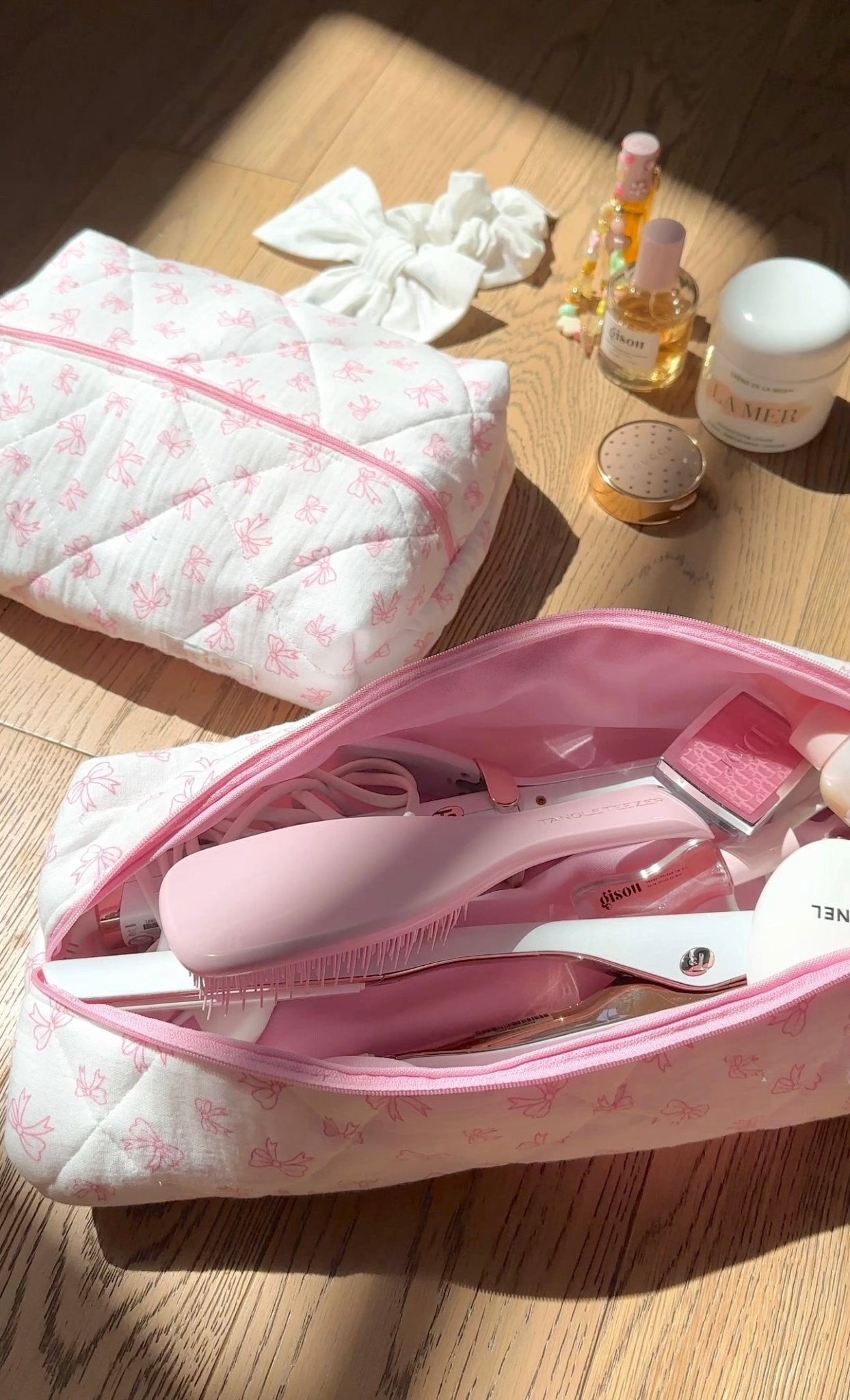 White quilted long hair tool bag with pink bow pattern and pink zipper, partially open.