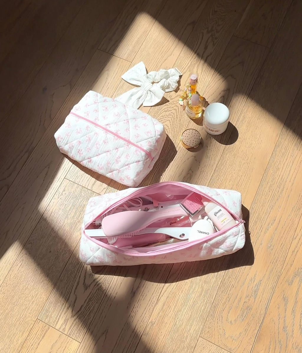 White quilted hair tool bag with pink bow pattern, open top with pink zipper and lining.