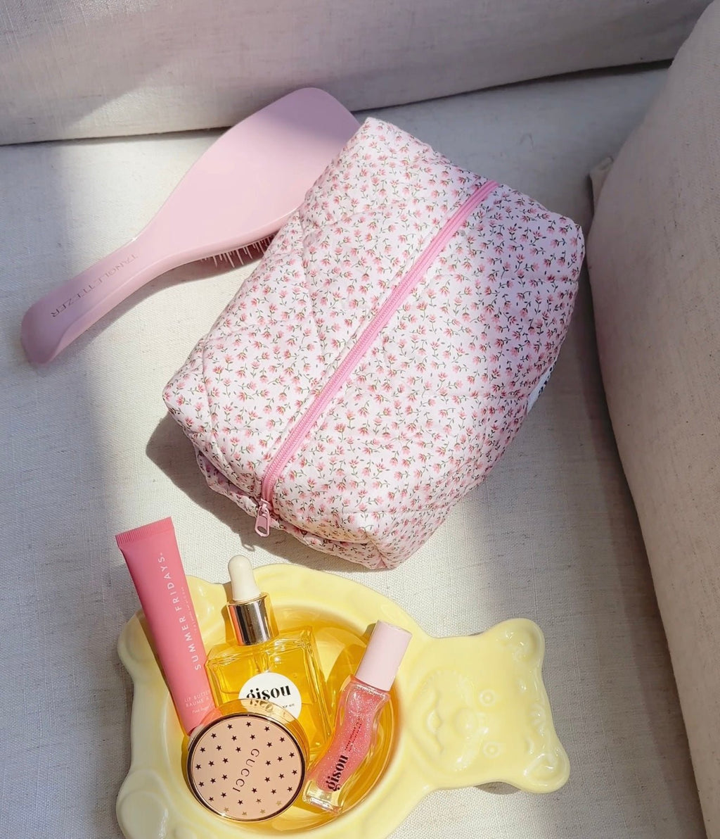 Pink ditsy floral toiletry pouch with pink zipper seam; partially filled items nearby.