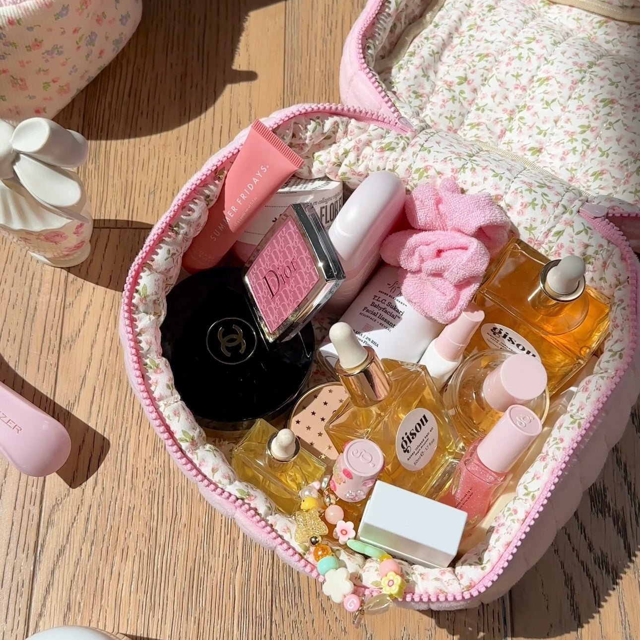 Open pink floral vanity bag with zipper edge, cushioned interior and dangling charm