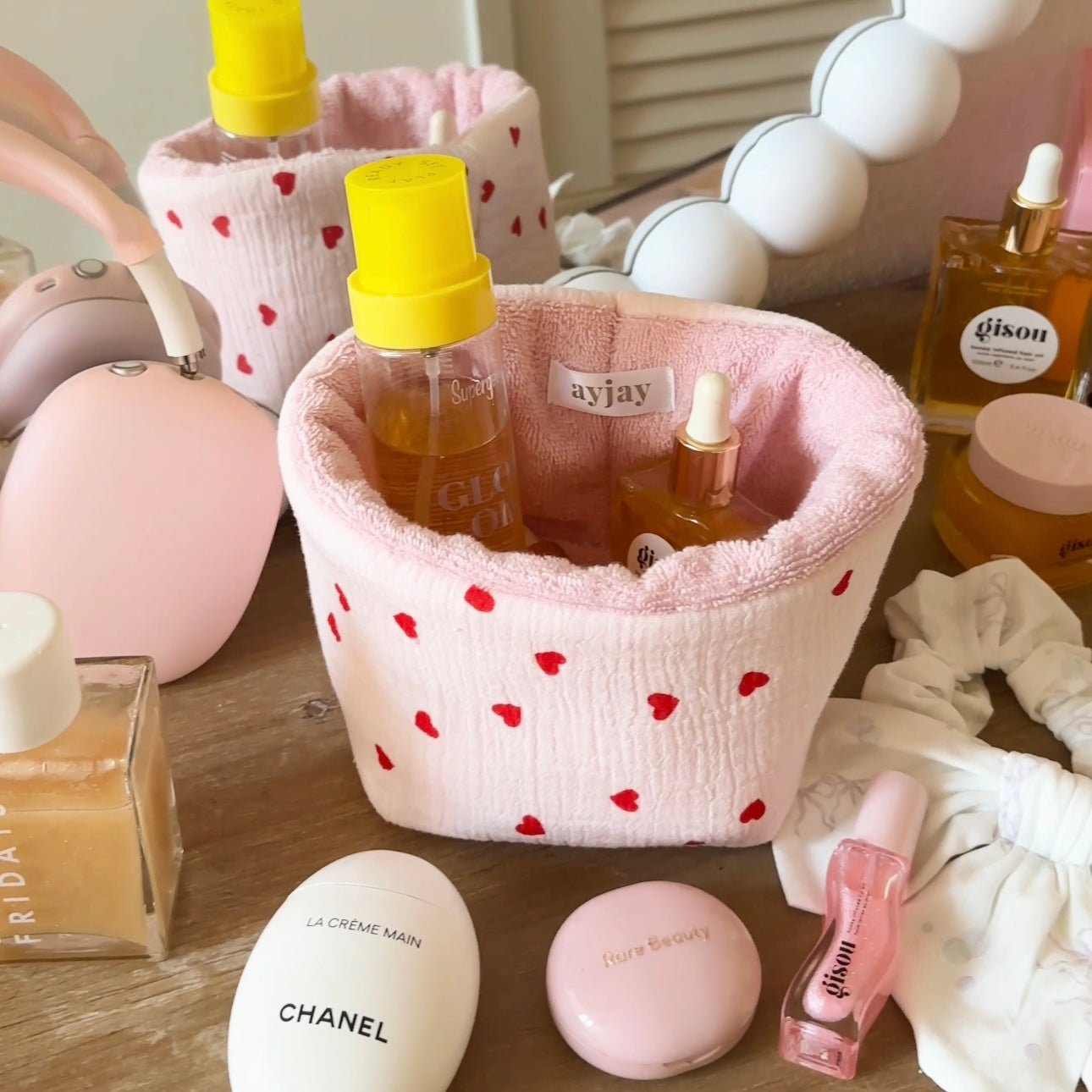 Pink fabric organizer pouch with red hearts print, open top holding bottles and tubes
