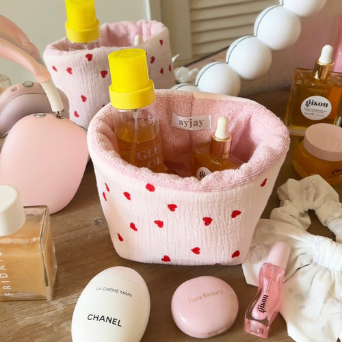 Pink fabric organizer pouch with red hearts print, open top holding bottles and tubes