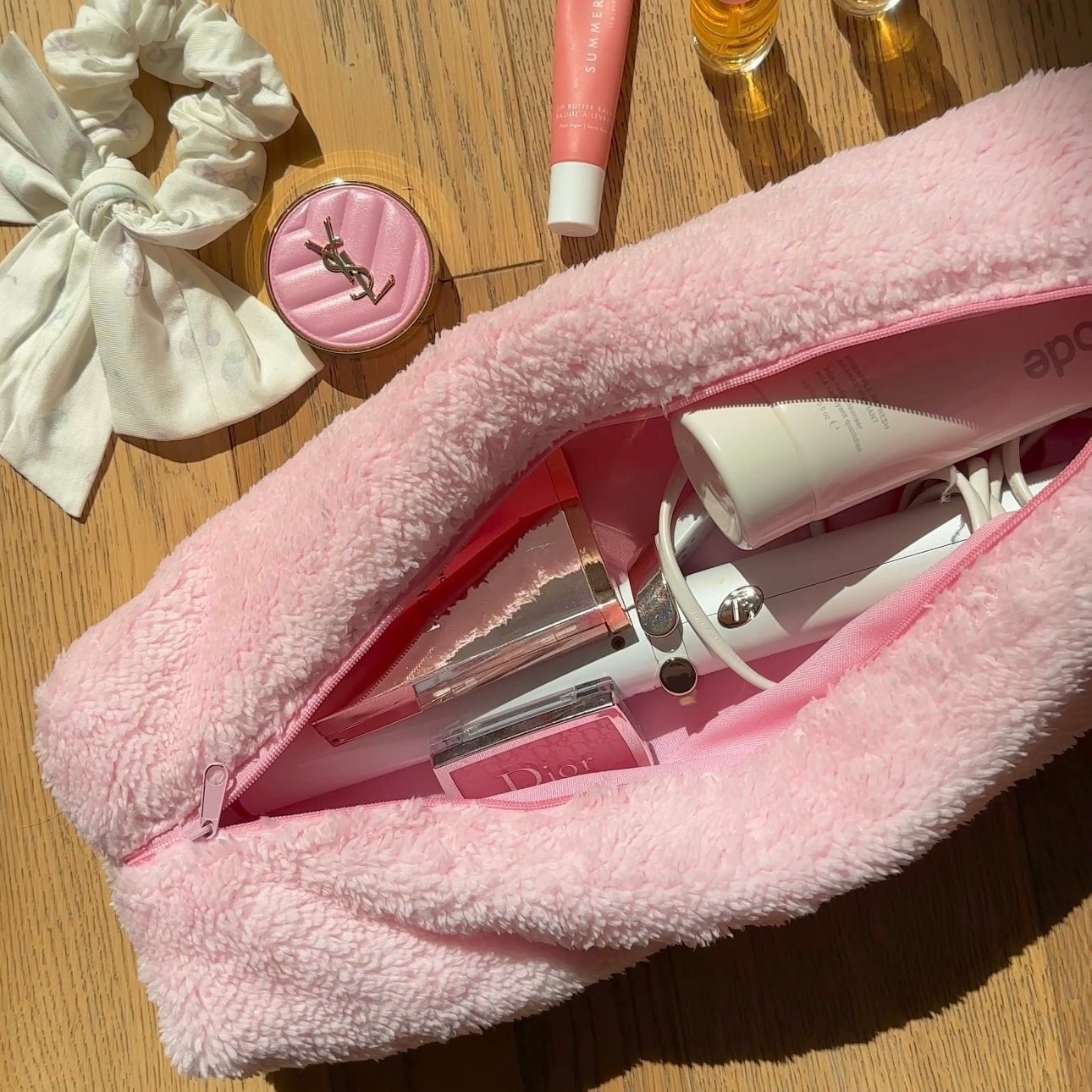 Light pink soft teddy zip pouch, open showing tubes and a spray bottle inside