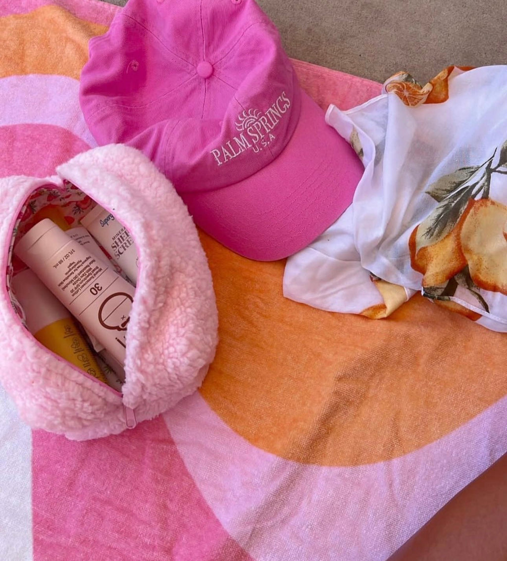 Pink teddy pouch with strawberry-lined pocket, open, with cosmetics inside.